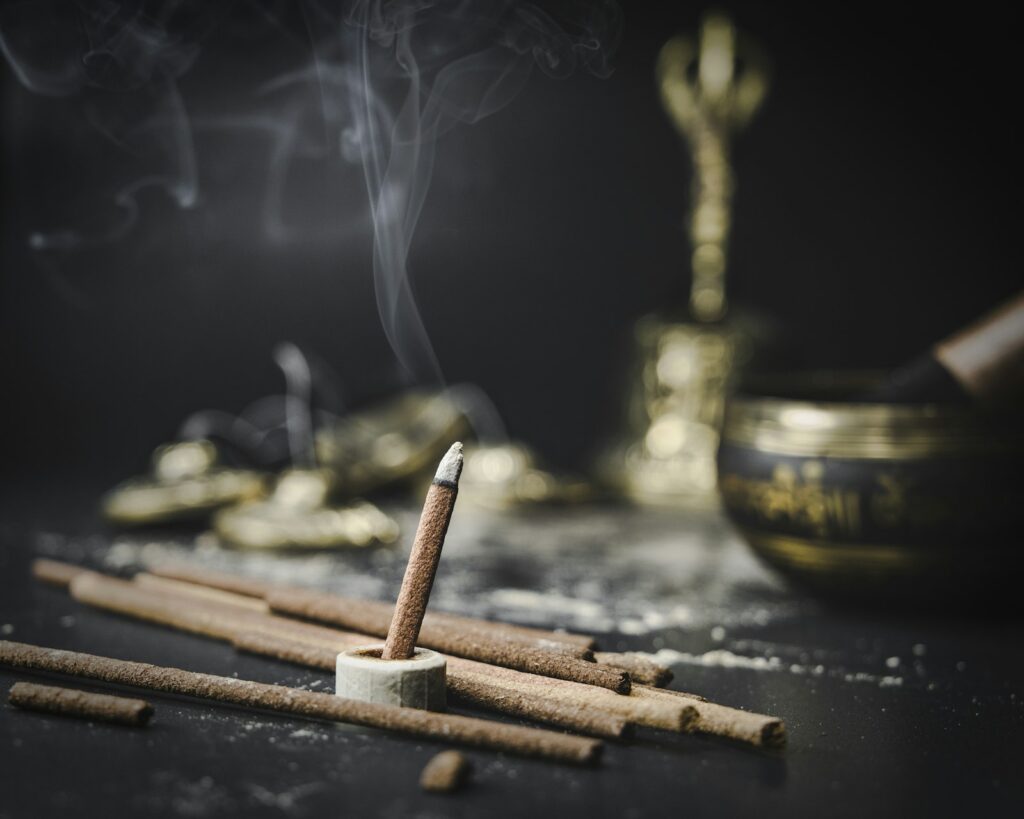 Incense sticks and aromatic wood beside a brass bowl, evoking oud and sandalwood base notes